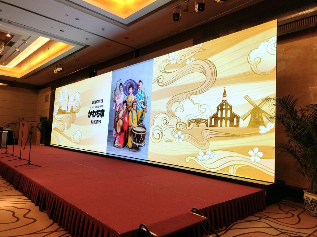 チンドンかわち家が長崎総領事館開設40周年記念祝賀会の大型デジタルサイネージにチンドンかわち家の映像が映っている